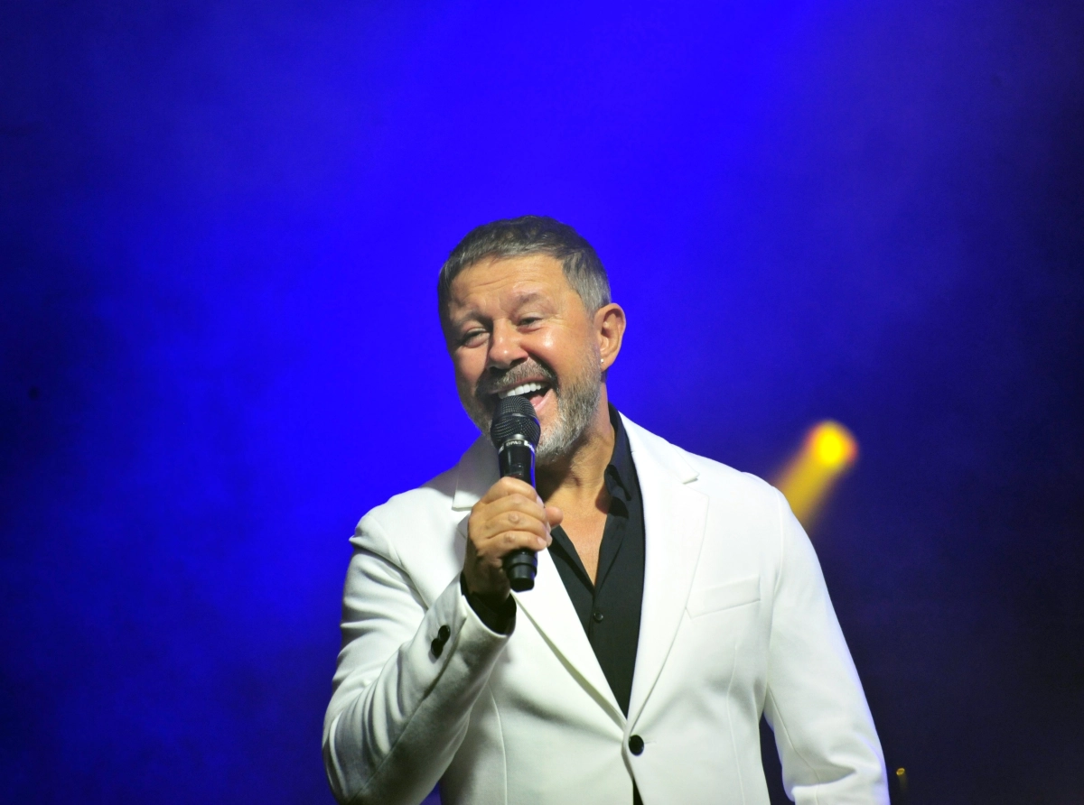 Andrzej Piaseczny podczas koncertu w Kościańskim Ośrodku Kultury, śpiewający na scenie w blasku reflektorów.